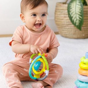 Rozesmáté miminko drží oběma rukama kulaté chrastítko ze sady hraček Box of Cheer